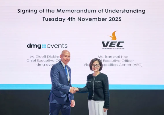 Two executives shake hands in front of a presentation screen announcing the November 2025 signing of a memorandum of understanding between dmg events and the Vietnam Exposition Center.