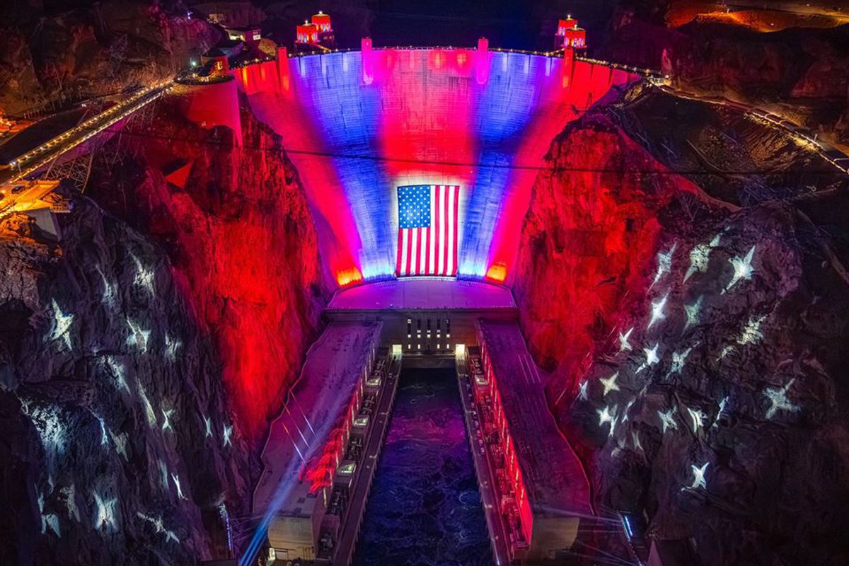 Hoover Dam lit in red, white, and blue with a large American flag.
