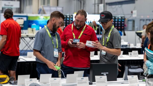 Three attendees review products and information on the ICAST tradeshow floor while wearing event badges.